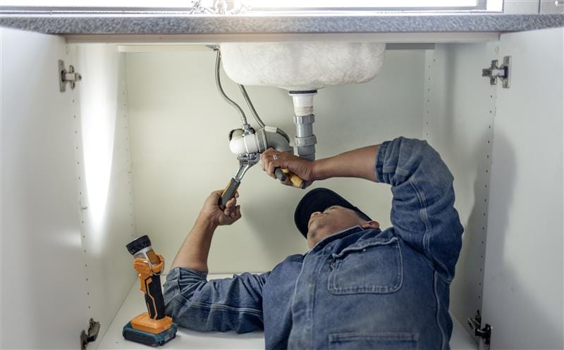 Plumber repairing pipes beneath a bathroom sink in Wellington