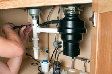Plumber repairing a garbage disposal beneath a kitchen sink in Wellington