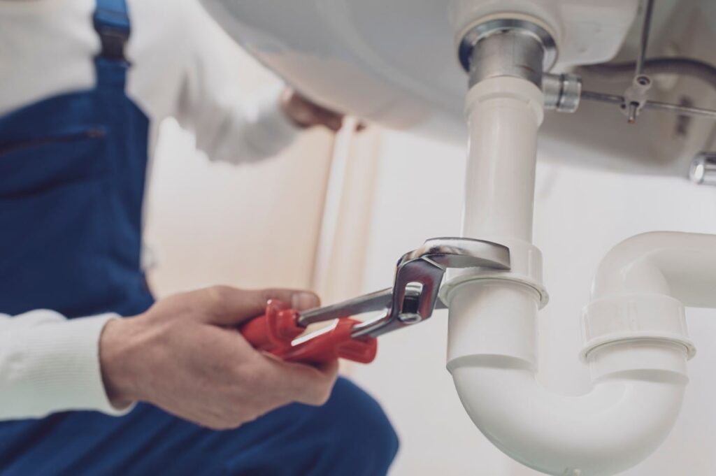 Plumber repairing a white drain pipe beneath a sink in Wellington