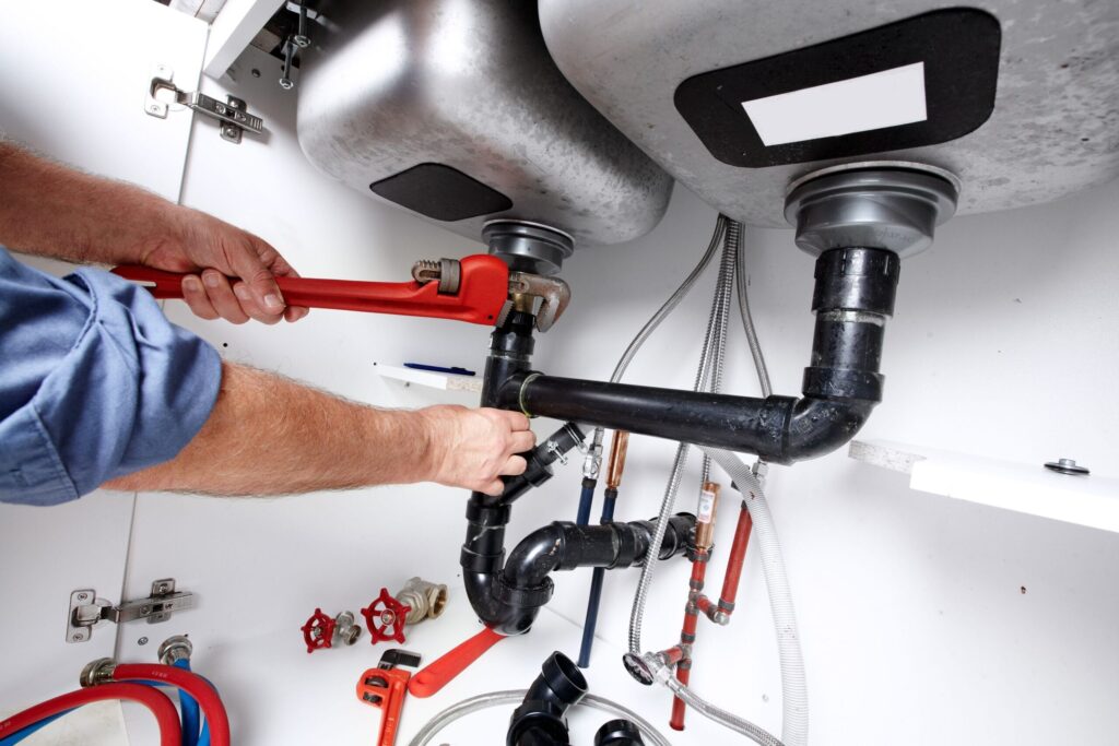Plumber repairing drain pipes beneath a kitchen sink in Wellington